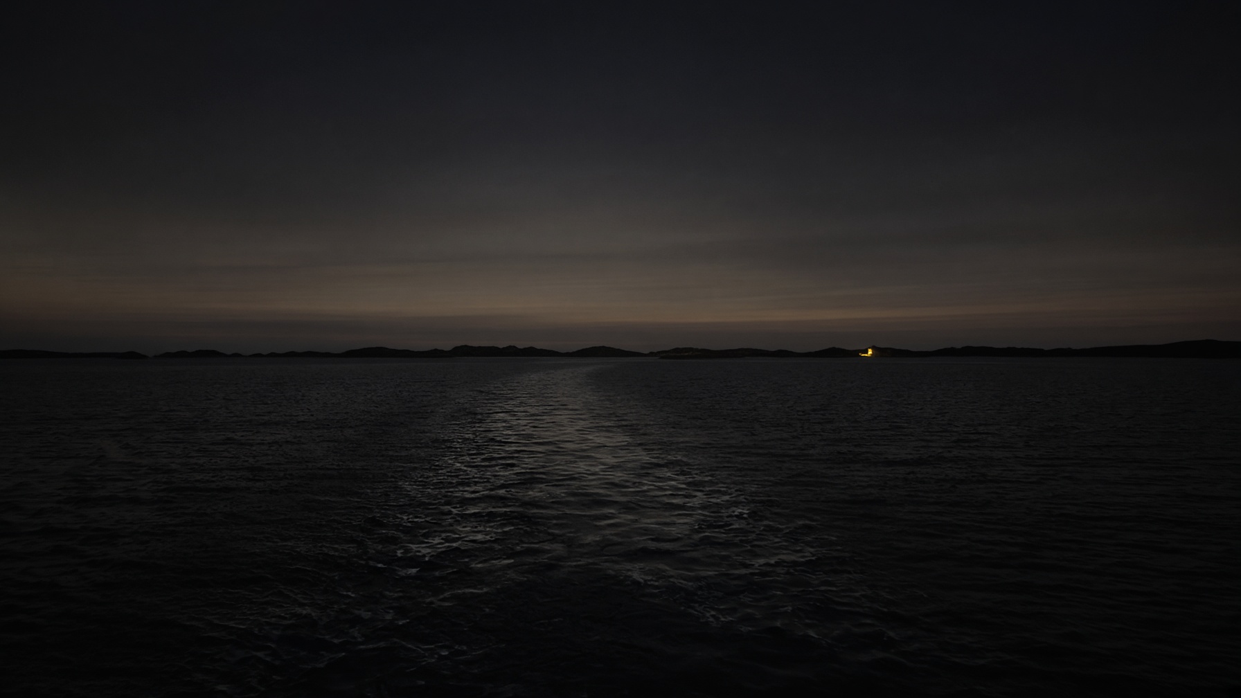 A dark sea at dusk. A faint coastline. One small lamp as if a house. The end of a long journey, not yet recognized.